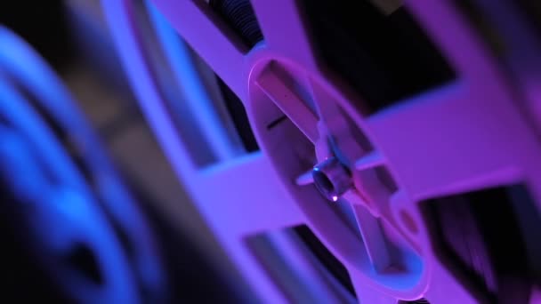 Старый 8-миллиметровый кинопроектор показывает пленку ночью в темной комнате с фиолетовым светом. Крупный план катушки. Медленное движение. — стоковое видео
