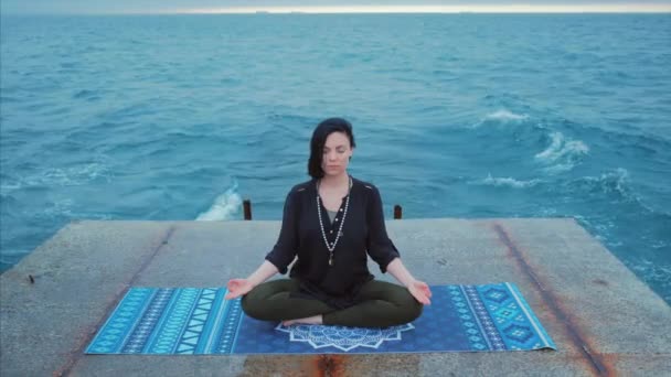 Διαλογισμός. Γιόγκα νεαρή ήρεμη μελαχρινή γυναίκα από τα κύματα θάλασσα στην προβλήτα χαλαρώνοντας σε γαλήνιο zen. lotus yoga ποζάρουν σε μια παραλία με συννεφιά. Όμορφο πολύχρωμο φόντο. 4ια — Αρχείο Βίντεο