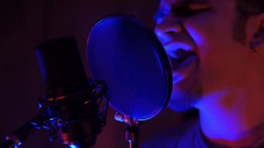 Etkileyici bir adam, bir stüdyoda, Neon ışığı ve duman makinesinin altında mikrofonda şarkı söylüyor.