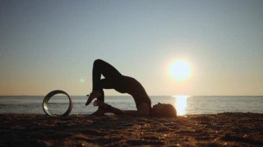 Kum Denizi sahilinde yoga tekeriyle sabah yogası yapan güzel bir kadının silueti. Yavaş çekim.