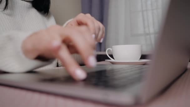 Primo piano della donna d'affari digitando sul computer portatile e beve caffè o tè. Mani femminili occupate a digitare sulla tastiera. Ragazza freelance che lavora a casa in inverno. Dolly, rallenta. — Video Stock