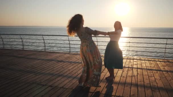 美しい女の子が旋回し、踊り、海や海の近くの堤防で遊んでいます。友情の概念、スローモーション — ストック動画