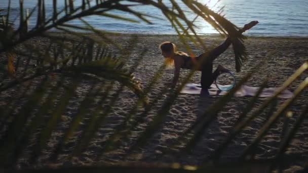 Silhueta de bela jovem praticando ioga matinal na praia de areia do mar com roda de ioga. Palmeira. Movimento lento. — Vídeo de Stock