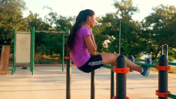 Mujer atlética joven haciendo flexiones en una barra horizontal en un día soleado de verano en el estadio, vista trasera. Movimiento lento. — Vídeos de Stock