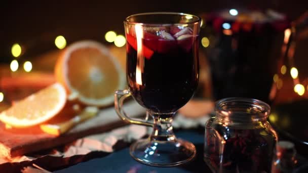 Natureza morta - vinho ruminado, vinho tinto quente com temperos no vidro entre frutos com luzes brilhantes de grinaldas. Celebração de Natal aconchegante perfumado, conceito de soco perfumado. — Vídeo de Stock