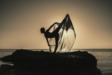 Esnek kadın jimnastikçi veya balerin, gökyüzünde ve deniz zemininde rüzgarda dalgalanan ipek kumaşla dans ediyor. Doğada şefkat, hafiflik, sanat ve yetenek kavramı
