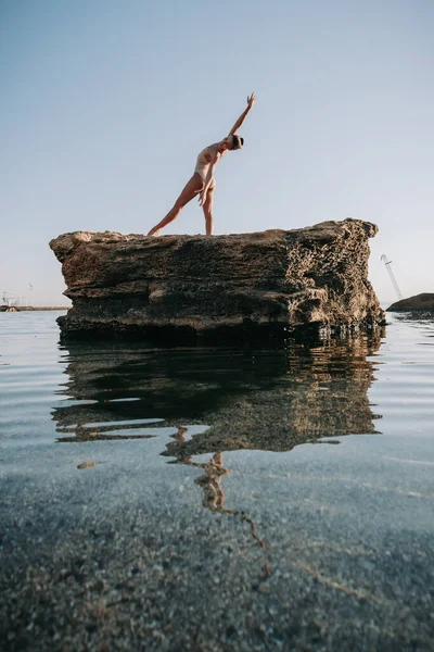 Jovem bailarina em maiô bege dançando balé no mar ou praia de areia oceânica na luz da manhã. Conceito de alongamento, arte, beleza da natureza. — Fotografia de Stock