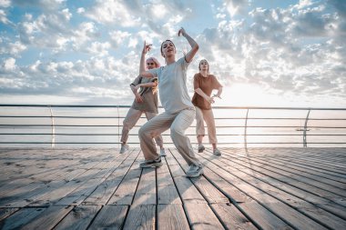 Dans eden genç kızlar hip-hop hareketlerinden hoşlanıyorlar. Modern kadınlar gün doğumunda deniz kenarında serbest dans ediyorlar..