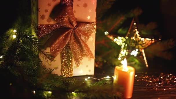 Fond de Noël - boîte cadeau élégante dorée avec arc. Bougie allumée et étoile brillante comme symbole des traditions. Bonnes vacances concept. — Video