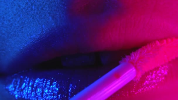 Egy nő, aki folyékony fényt vagy rúzst használ a szexi ajkain. Villogó, színes neon fény. Extrém közelről érzéki női arc. Reklám smink, szépség, kozmetikai koncepció