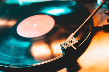Görüntü yönetmeni vinil plak çalar ve müzik plakası boyunca uzanan bir pikap. Neon ışığı. Retro-stil dönen plak çalar. Kapat.