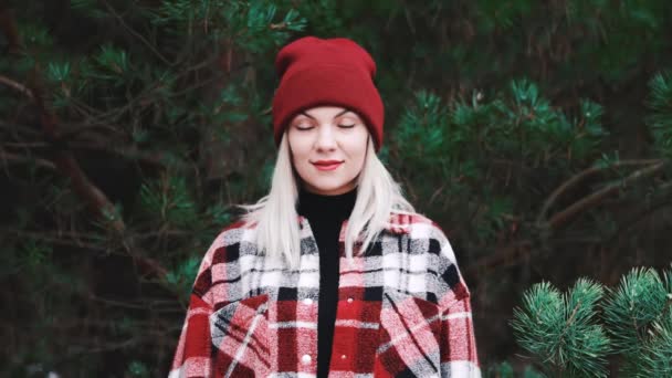 Retrato de una joven mujer bonita en el bosque, temporada de invierno. Muchacha amable atractiva sonriendo, señora en camisa de moda y sombrero de gorro rojo. — Vídeos de Stock