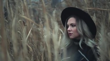 Düşünceli ve şapkalı küçük üzgün hippi kadının portresi sonbahar sonbaharı arka planında sazlıklar arasında poz veriyor. Harika bir stil kızı. Otantik boho görüntüleri 