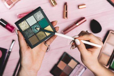 Pembe düz kozmetik koleksiyon arka planında yeşil göz farı paletiyle çalışan bir kadın. Güzellik endüstrisindeki aletler - ruj, allık, parlaklık. 