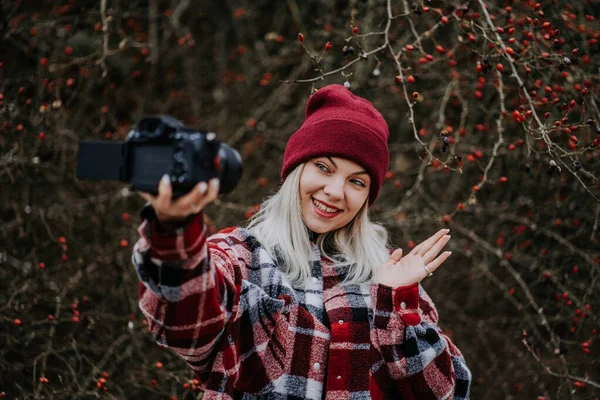 Sorridente donna blogger di viaggio facendo nuovo video blog, vlog, con la sua fotocamera sullo sfondo della foresta naturale. Influencer parlare con la fotocamera e sorridente. — Foto Stock
