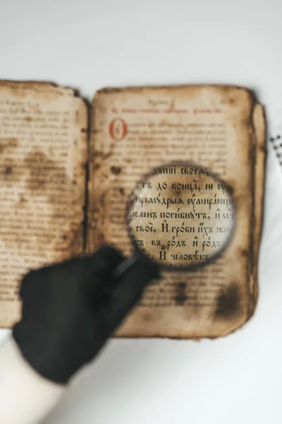 Historiador científico en guantes leyendo libro antiguo con lupa. Traducción de literatura religiosa. Manuscrito con escritos antiguos. Tesoros del pasado. Pieza del museo. — Foto de Stock