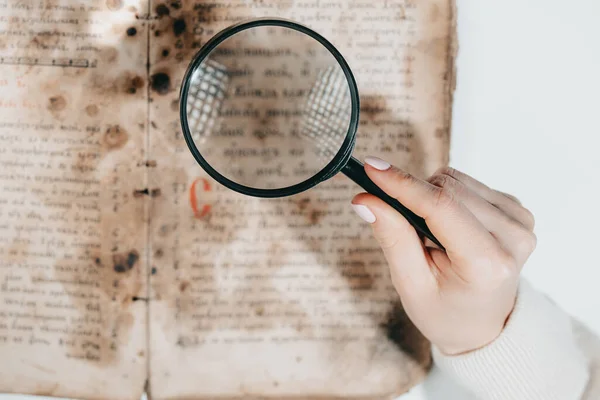 Mujer investigadora explora libro antiguo con lupa. Traducción científica de la literatura. Investigando manuscrito con escritos antiguos —  Fotos de Stock