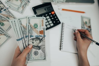 Tanımlanamayan bir kadın elinde para tutuyor ve hesap makinesinin gelirini hesaplıyor. Ev bütçesi ve harcamalarının takibi. Muhasebeci ya da bankacı çalışıyor - üst görünüm.