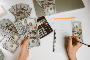 Tanımlanamayan bir kadın elinde para tutuyor ve hesap makinesinin gelirini hesaplıyor. Ev bütçesi ve harcamalarının takibi. Muhasebeci ya da bankacı çalışıyor - üst görünüm.