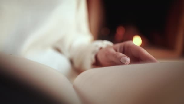 Mujer en blanco leyendo interesante libro de papel mientras está sentada cerca de la chimenea en casa. Acogedor video de invierno de la señora relajándose sola con la novela. — Vídeos de Stock