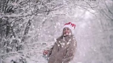 Noel Baba şapkalı neşeli tatlı kadın ağacın dalını çeker, üstünde kar uçar ve kışın ve soğuk havanın keyfini çıkarır. Yavaş çekim.