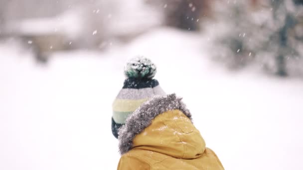 Adorabile ritratto di ragazzo bambino felice su sfondo neve invernale. Bambino in parka giallo gioisce prima neve. Rallentatore. — Video Stock