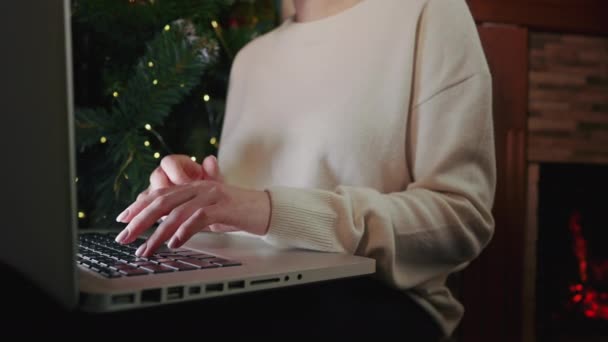 Jovem estudando no laptop, sentado perto da lareira aconchegante em casa. Concentre-se em mãos digitando no teclado. Conceito de distanciamento social. Senhora escrevendo mensagem aos amigos. — Vídeo de Stock