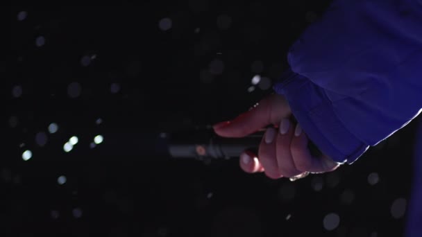 La mano femenina sostiene la linterna y brilla por la noche, buscando algo. Invierno, nevada, ventisca, temperatura fría. — Vídeos de Stock