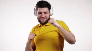 Beyaz arka planda kulaklıkla dans eden sakallı yakışıklı bir adam. Müzik, aktif dans, radyo konsepti, yavaş çekim