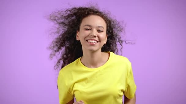 Молода мила жінка посміхається і танцює на фіолетовому студійному фоні. Дівчина в яскраво-жовтому одязі. Позитивний настрій. Повільний рух . — стокове відео