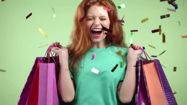 Podekscytowana kobieta z kolorowymi papierowymi torbami po zakupach przeskakując konfetti deszczu w tle studio. Koncepcja sezonowej sprzedaży, zakupów, wydawania pieniędzy na prezenty — Wideo stockowe