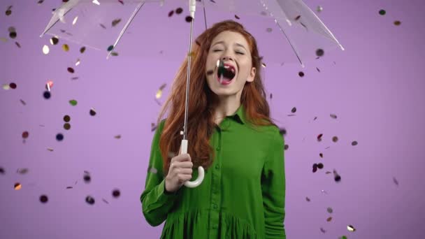Glückliche Frau steht unter Regenschirm, freut sich über Konfettiregen im violetten Atelier. Konzept Wow-Idee, feiern, feiern, gewinnen
