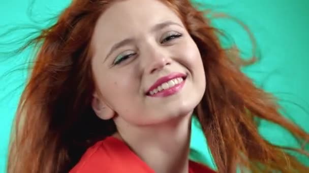 Nära porträtt av rödhårig kvinna leende och dans på studio bakgrund. Flicka i orange ljus klädsel. Positivt humör. Långsamma rörelser. — Stockvideo