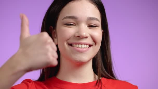 Nette Frau zeigt Daumen nach oben Zeichen über violetten Hintergrund. Positives junges Mädchen lächelt in die Kamera. Sieger. Mit Erfolg. Körpersprache. — Stockvideo