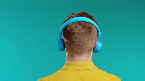 ヘッドフォンで音楽を聴いている認識できない男、青い背景でスタジオで踊る男。無線技術、無線概念. — ストック動画