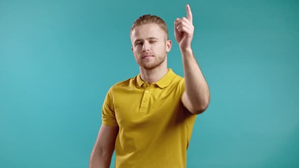 Charmant homme pointe index dans l'objectif de la caméra et clins d'oeil, flirts. Hé, toi Guy en t-shirt jaune sur fond bleu. — Video