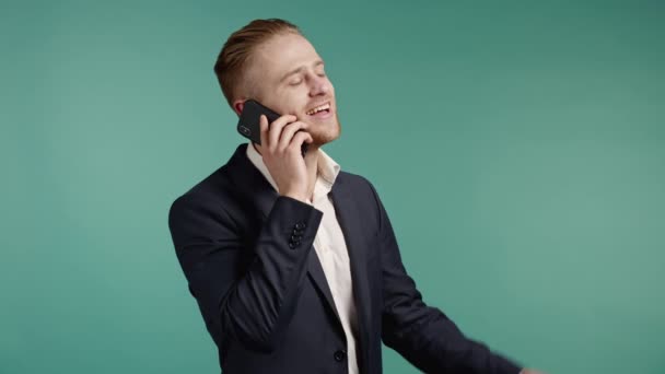 Jovem empresário fala com sorriso no telefone. Cara segurando e usando smartphone. Roupa de fato. Azul estúdio fundo. — Vídeo de Stock