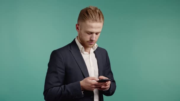 Beau homme d'affaires utilisant un smartphone sur un mur de studio bleu. Technologie moderne - applications, réseaux sociaux. — Video