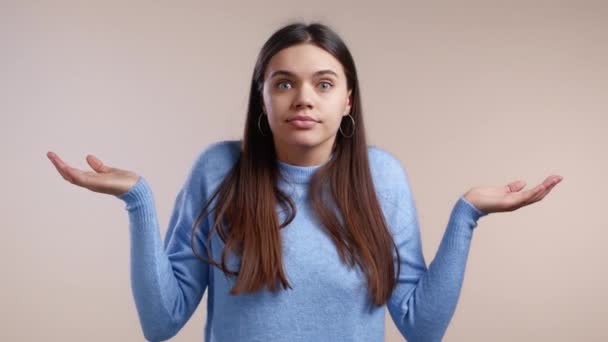 Joven indiferente mujer insegura hace gesto de que no sé, no puedo ayudar en nada. Concepto de pregunta difícil. Fondo de estudio blanco. — Vídeos de Stock