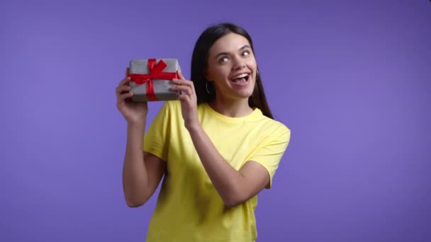 Heyecanlı kadın fiyonklu hediye kutusu aldı. O mutlu ve ilgiyle pohpohlanıyor. Menekşe arkaplanda gülümseyen bir kız. Stüdyo resmi — Stok video