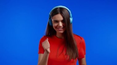 Mavi stüdyo arka planında kulaklıkla dans eden çekici bir kadın. Şirin kızlar portresi. Müzik, radyo, mutluluk, özgürlük, gençlik kavramı.