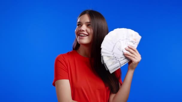 Sourire femme heureuse avec de l'argent comptant - USD dollars billets de banque sur le mur bleu. Symbole de jackpot, gain, victoire, gagner à la loterie — Video
