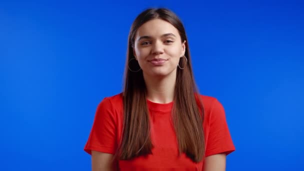 Jonge mooie vrouw met lang kapsel op zoek naar camera, flirten. Mooi model meisje in oranje op blauwe studio achtergrond. — Stockvideo