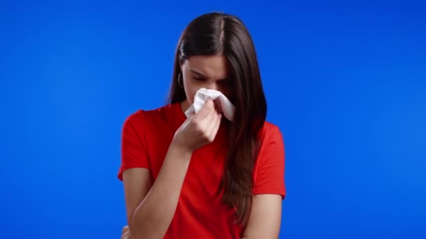 A mulher espirra para o tecido. Menina isolada no fundo do estúdio azul. A senhora está doente, tem uma reacção fria ou alérgica. 2021 doença, epidemia, vírus da imunodeficiência — Vídeo de Stock