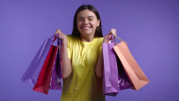 Ενθουσιασμένη γυναίκα με πολύχρωμες χάρτινες σακούλες μετά τα ψώνια σε βιολετί φόντο στούντιο. Έννοια της εποχιακής πώλησης, αγορές, δαπάνες χρημάτων για δώρα — Αρχείο Βίντεο