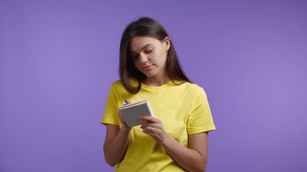 Leuke vrouw schrijft toekomstplannen en to-do lijst in notitieboekje voor week of maand. Ze maakt notities in de planner, meisje met pen. Persoonlijk dagboek bijhouden over violette studio achtergrond. — Stockvideo