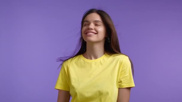 Привлекательная женщина флиртует, позирует на фоне фиолетовой студии, ее длинные волосы трепещут от воздушного потока. Девушка в ярко-желтой одежде. Позитивное настроение. Медленное движение — стоковое видео