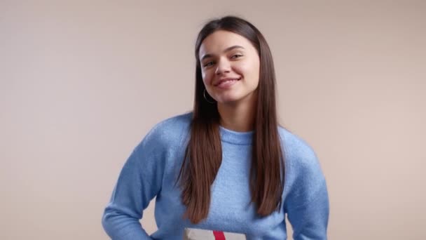 Mujer da caja de regalo a mano a la cámara en el fondo de la pared de luz. Chica sonriendo, ella es feliz con el presente, asiente con la cabeza, es para usted. Retrato de estudio — Vídeos de Stock