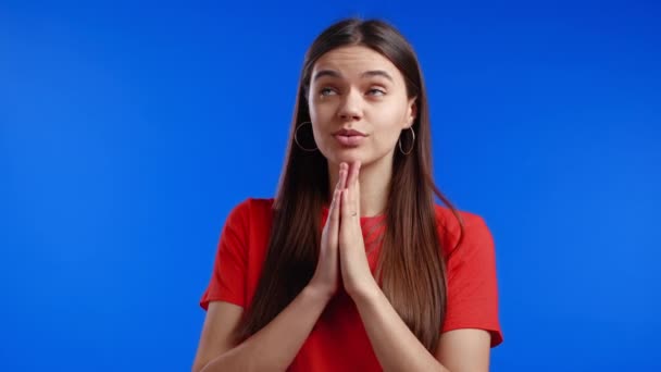 青い背景の上で祈るオレンジのTシャツの美しい女性。夢を叶えるために神に懇願する女の子,助けて. — ストック動画