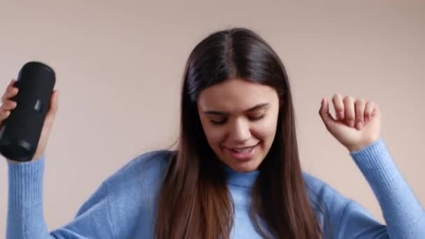 Woman listening to music by wireless portable speaker - modern sound system. Young girl dancing, enjoying on beige studio background. She moves to the rhythm of music. — Stock Video